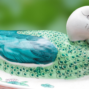 a blue and green ceramic duck against a blurred garden background.