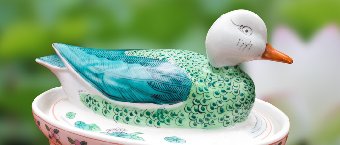 DUCK a blue and green ceramic duck against a blurred garden background.