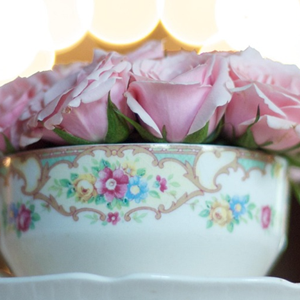 pink roses in a decorated tea cup. with a blurred light behind them.